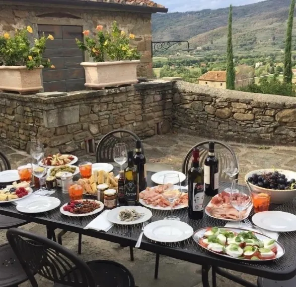 Outdoor table set with assorted appetizers, wine, and bread in a rustic courtyard.