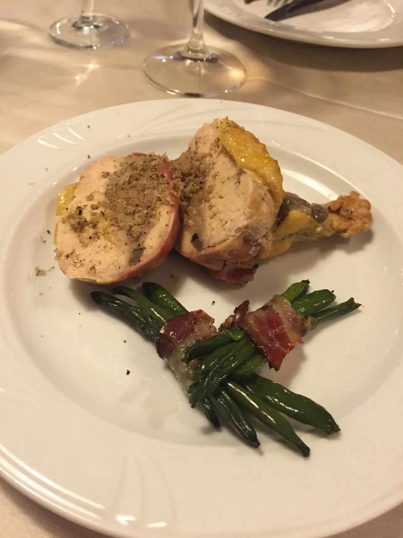Stuffed chicken breast with green beans wrapped in bacon on a white plate.
