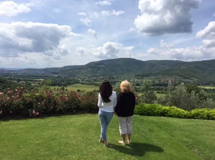 Two women standing on a lawn overlooking a scenic mountain landscape.